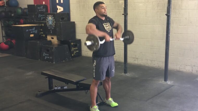 Muscular person in gym lowering barbell from shoulders