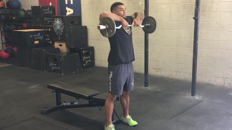 Muscular person in gym lifting barbell to shoulders