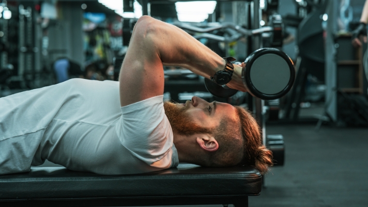 Person in white lying on gym bench holding a dumbbell overhead.