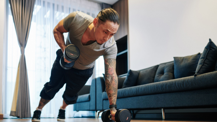 tattooed person in home gym doing dumbbell row exercise on floor