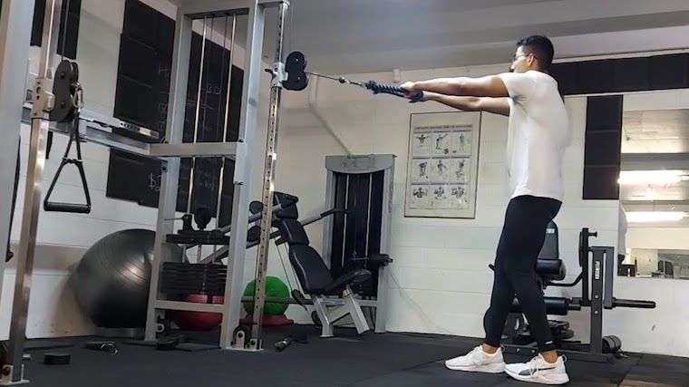 person in gym doing standing cable row execise