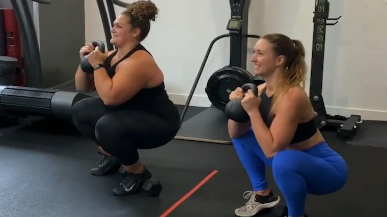 two people in gym doing kettlebell squat