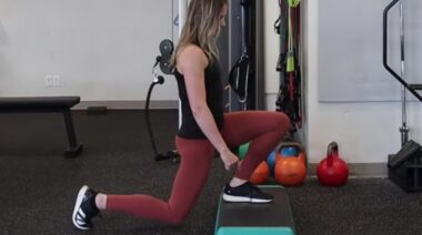 Long-haired person in gym doing single-leg lunge exercise