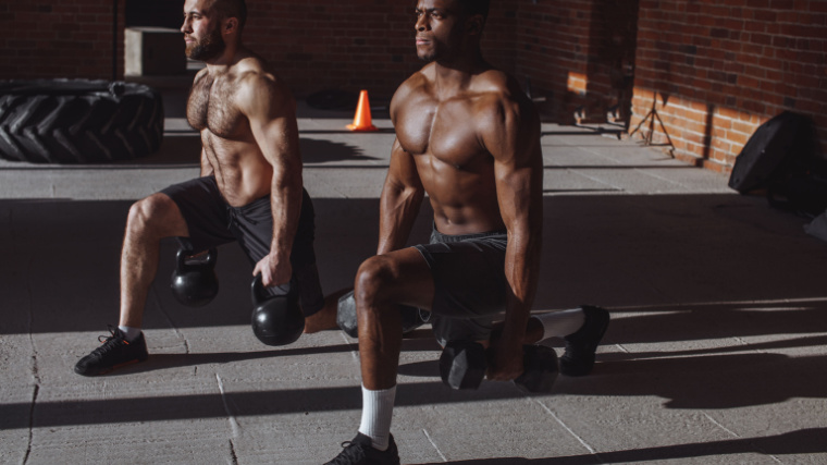 Two muscular lifters in gym doing kettlebell lunge