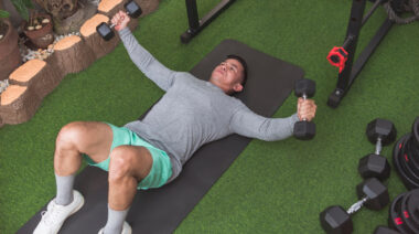 Muscular person on floor doing dumbbell chest exercise