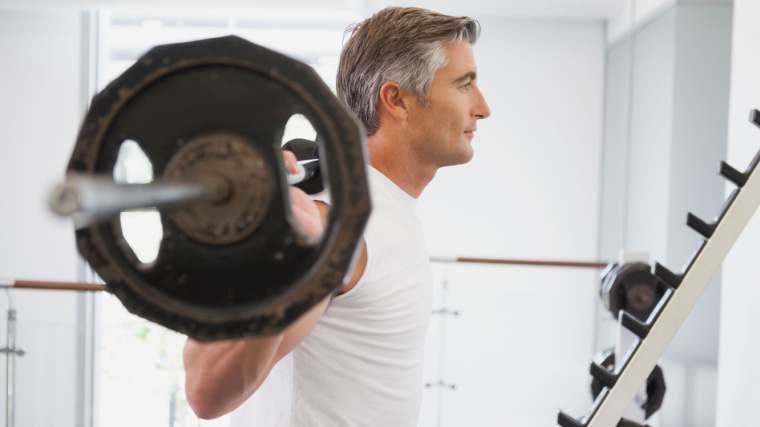 gray-haired person in gym doing barbell squat