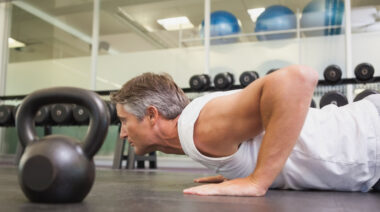 gray-haired person in gym doing push-ups on floor