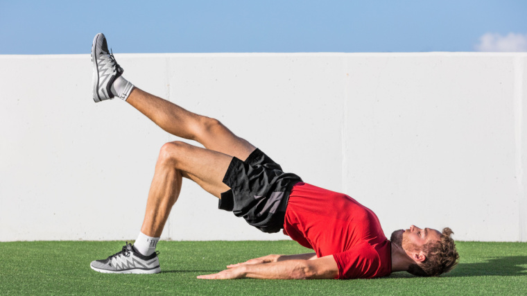 Muscular person outdoors on ground doing leg exercise