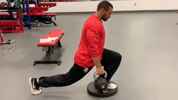 Person in gym doing single-leg lunge with kettlebell