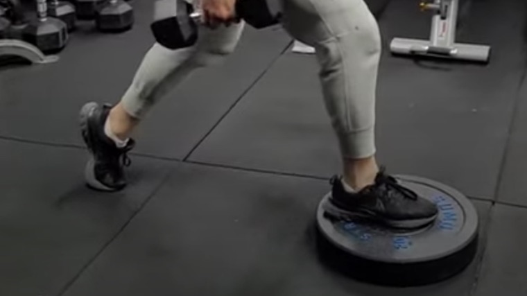 person in gym elevating one foot on weight plate