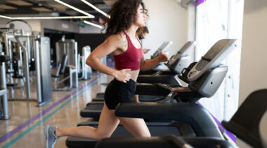 Long-haired person in gym running on treadmill