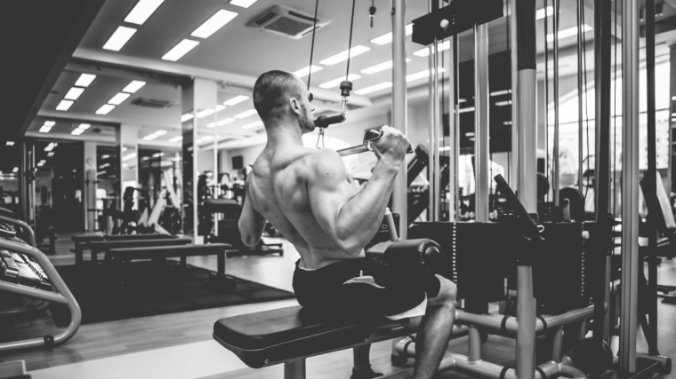 Muscular person in gym doing lat pulldown exercise