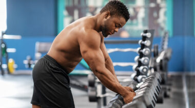 muscular person in gym grabbing dumbbells