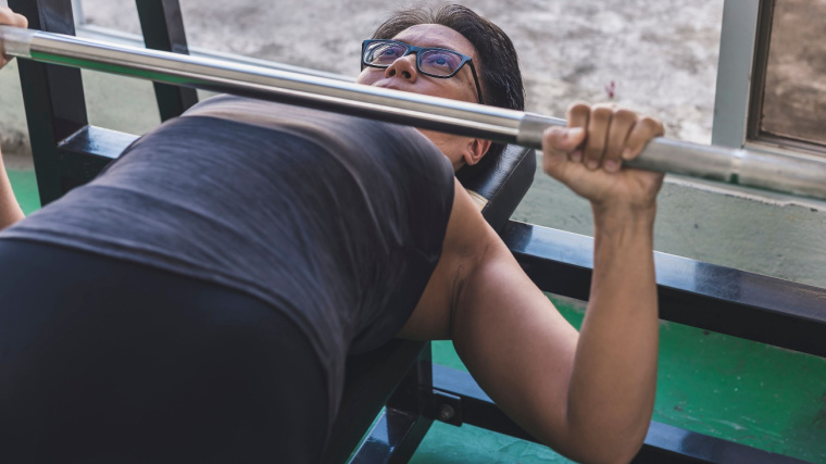 short-haired person in gym doing barbell bench press