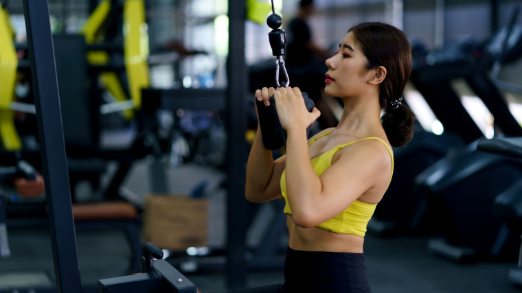 Long-haired person in gym doing pulldown exercise