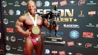 Bodybuilder David Henry flexing muscles while holding trophy