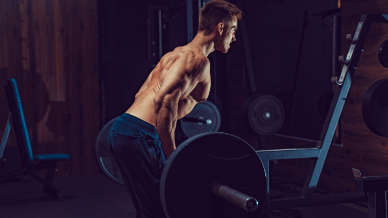 muscular person in gym rowing barbell