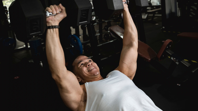 muscular person in gym doing incline dumbbell press