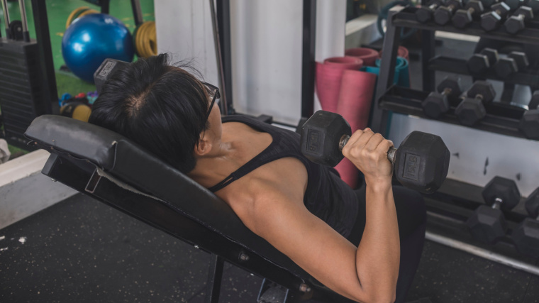 Short-haired person in gym doing incline dumbbell press