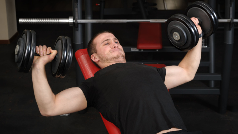 person in gym struggling with dumbbell press