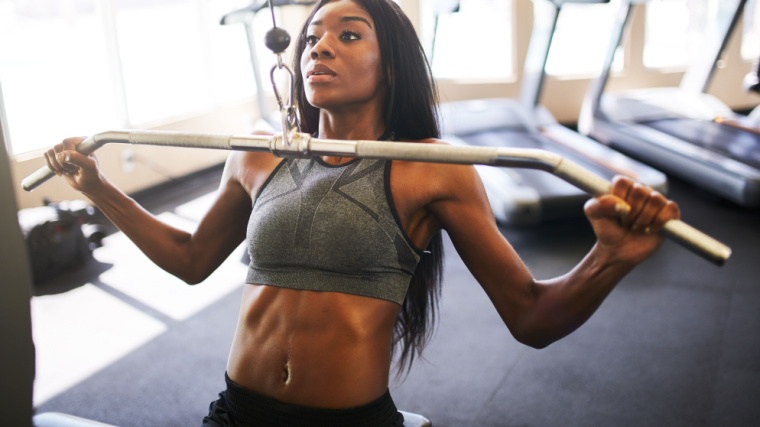 Long-haired person in gym doing lat pulldown exercise