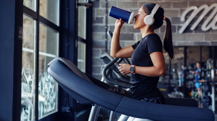 Long-haired person running on treadmill while drinking protein shake