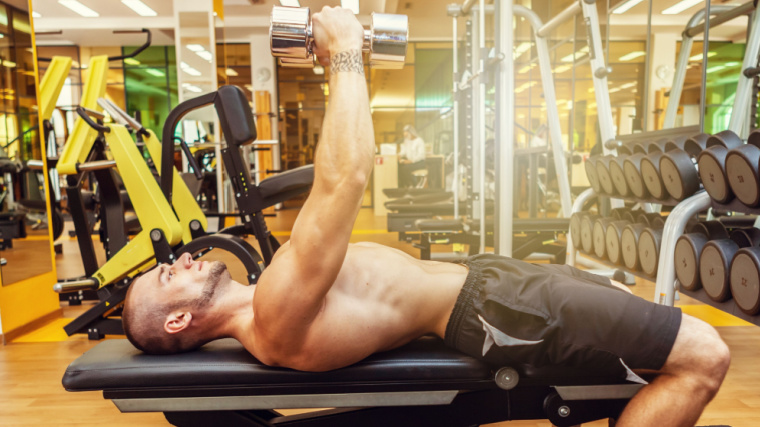 Shirtless person in gym doing dumbbell chest exercise