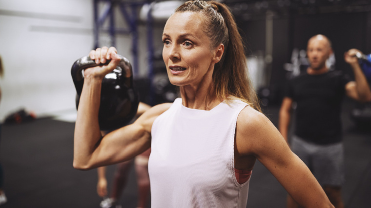 Long-haired person in gym doing kettlebell shoulder press