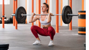 Long-haired person in gym doing barbell front squat