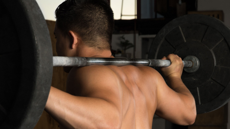 Shirtless muscular person in gym doing barbell squat