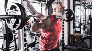 gray-haired person in gym squatting with barbell
