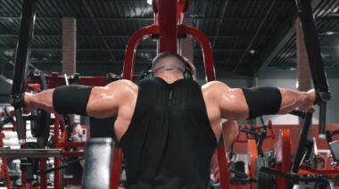 Bodybuilder Derek Lunsford performing shoulder raise exercise on machine in gym