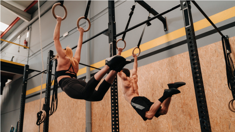 Two people in gym performing ring pull-ups