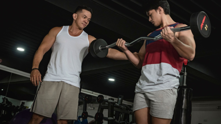 Two muscular people in gym performing barbell curl