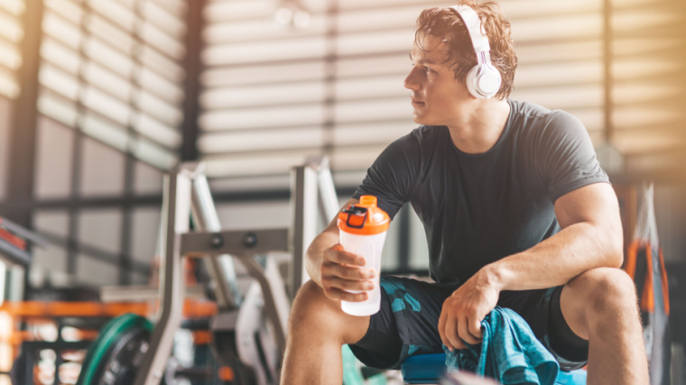 Sweaty person sitting in gym drinking protein shake