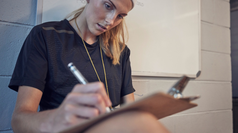 Long-haired person sitting down writing on clipboard