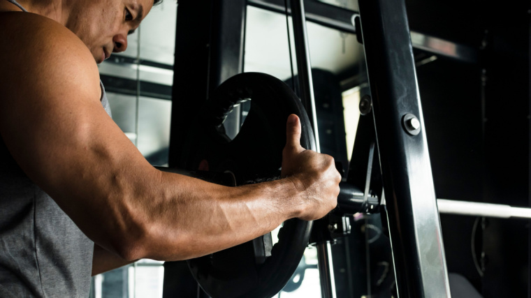 Muscular person putting weight onto machine in gym