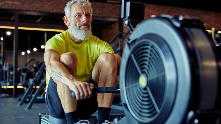 Grey-haired person in gym using rowing machine