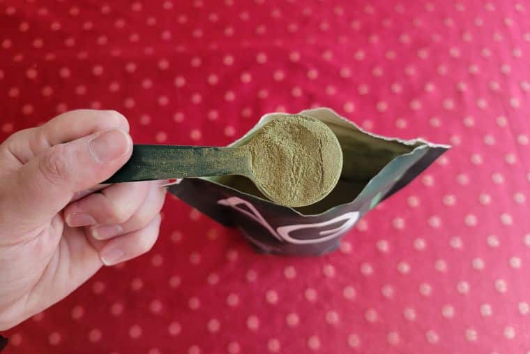 A woman's hand holding a scoop of AG1 Athletic Greens