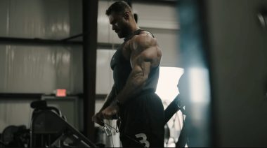 Chris Bumstead performing cable lateral raises in the gym.