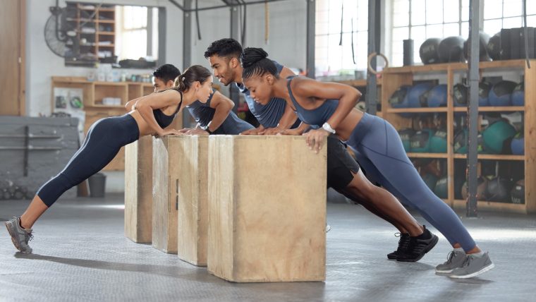 A group of people perform incline push-ups on plyo boxes.
