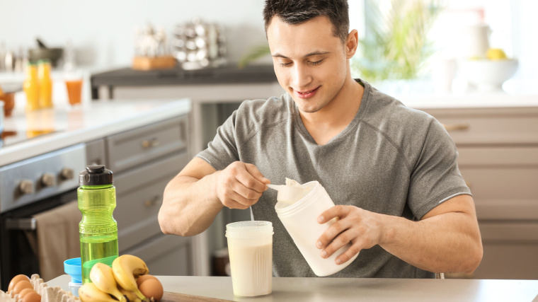 Muscular person in kitchen mixing protein shake