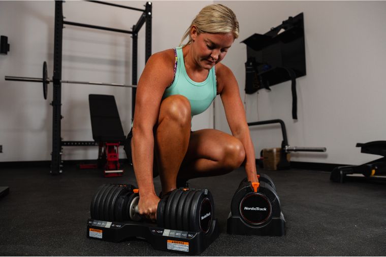 A young woman bending down to pick up the NordicTrack Select-a-Weight Dumbbells