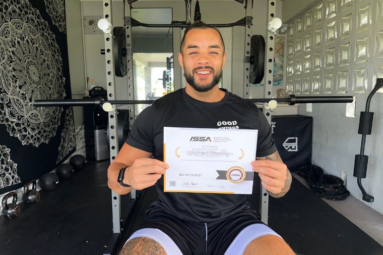 A young man setting in a gym holding his ISSA Nutritionist certificate