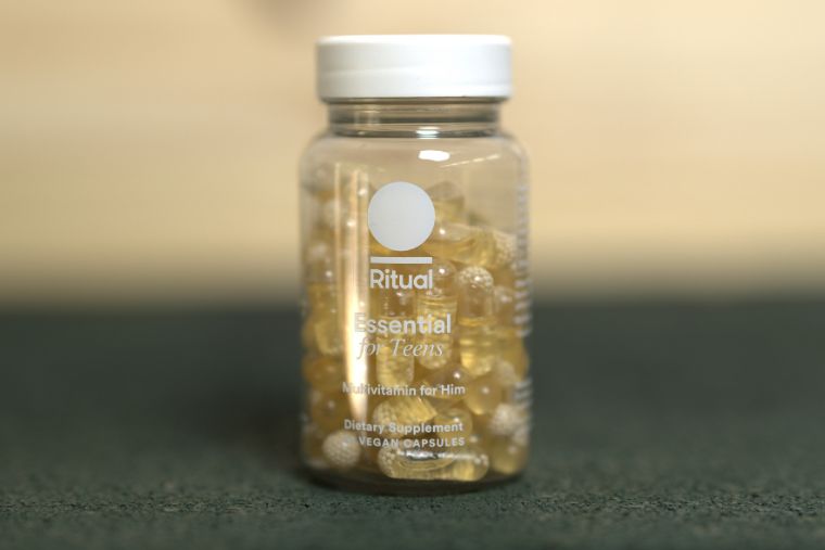 A bottle of Ritual's multivitamins for male teenagers in front of a wood background