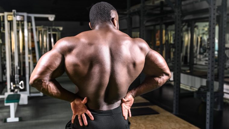 Bodybuilder flexes his back muscles while posing in the gym.
