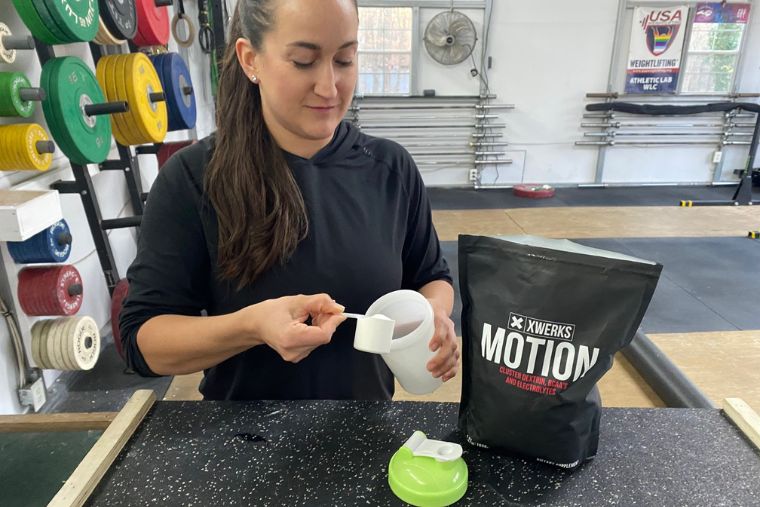A female athlete pouring a scoop of XWERKS Motion into a water bottle