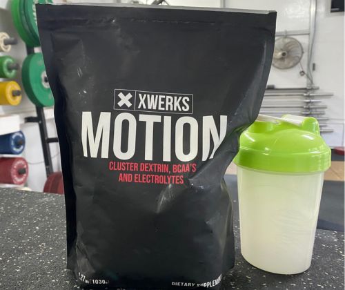 A bag of XWERKS Motion alongside a shaker bottle in an individual's gym