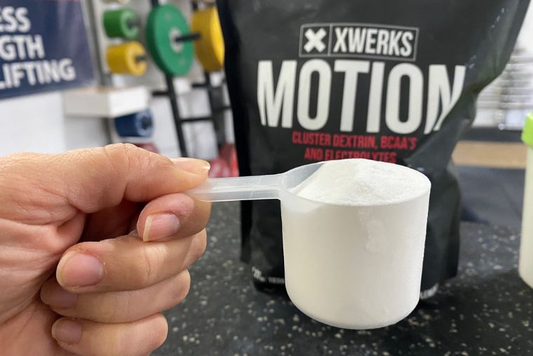 A hand holding a scoop of XWERKS Motion with the bag in the background