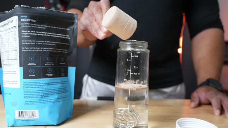 Man pouring a scoop of Legion Whey+ protein into a water bottle.